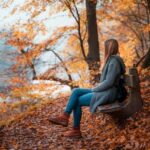 Девушка сидит на лавке посреди осенней листвы