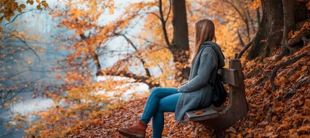Девушка сидит на лавке посреди осенней листвы
